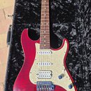 Elektrokytara s červeným tělem z plamenového javoru a krčkem z tmavého dřeva. Na hlavě je nápis "Sabo". Kytara má bílý pickguard, tři snímače typu si…