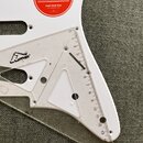 Detail bílého kytarového těla s nalepeným červeným kulatým štítkem s nápisy Fender, FREE ONLINE LESSONS*, FOR GUITAR, BASS AND UKULELE a START YOUR T…