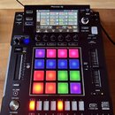 Černý sampler Pioneer DJ DJS-1000 s podsvícenými padovými políčky v různých barvách. Na horní straně je umístěn displej s ovládacími prvky a nápisy,…