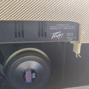 Detail zadní části kytarového komba s černým šasi a reproduktorem. Na kovovém panelu je bílý nápis A PRODUCT OF PEAVEY ELECTRONICS CORP. MERIDIAN, MS…
