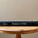 Černý digitální syntetizátor s klávesami v bílo-černé kombinaci. Na přední straně je bílý nápis Roland D-50 a řada ovládacích tlačítek a posuvníků. N…