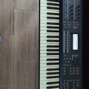 Černý klavír s bílými a černými klávesami. Na horní části je logo YAMAHA a v dolní pravé části nápis MOX6. Nástroj obsahuje displej, několik posuvník…