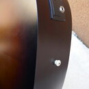 Detail zadní strany kytary v tmavě hnědé barvě. Je zde vidět černý plastový panel s integrovaným jack konektorem. Niže se nachází malý bílý plastový…