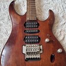 Elektrická kytara s hnědým dřevěným povrchem a tmavým hnedým hmatníkem. Nástroj má tři humbuckery, jeden ovládací knoflík hlasitosti a páčkový systém…