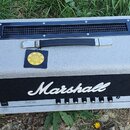 Kytarový zesilovač značky Marshall v šedém provedení s černým předním panelem. Na spodní liště je uveden nápis JCM 25/50 MODEL: 2555. Na horní straně…