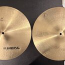 Dvě mosazné činely s jemným rýhováním povrchu. Levý činel nese nápisy „Byzance“ a „MEINL HOLANG MEINL“. Pravý činel nemá žádný viditelný nápis ani lo…