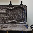 Otevřený tvrdý kufr na hudební nástroj s vnitřním polstrováním z šedého plyšového materiálu. Vnitřní prostor je tvarován pro kytaru nebo podobný nást…