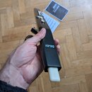 Černý, úzký elektronický přístroj s bílým zakončením na spodní straně. Na boku je viditelné logo AKAI Professional. V pozadí na podlaze leží dva papí…