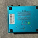 Zadní strana modrého elektronického zařízení s kovovým povrchem. Na zadní straně je bílý štítek s číslem 31440204481 a text v sekci CAUTION týkající…
