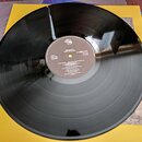 Černá vinylová deska položená na žlutém papírovém obalu. Bílý středový štít obsahuje nápisy MEGADETH / RUST IN PEACE, 21 0880-1 311 a SIDE 1 STEREO.…