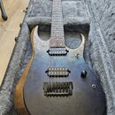 Elektrická kytara s tmavým, mramorovaným povrchem těla a hnědým drevem na hranách, položená v šedém plišovém kufru. Nástroj má dva humbuckery, černý…