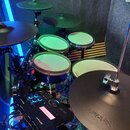 Elektronická bicí souprava s černým rámem a padovými bubny v bílo-zeleném provedení. Na modulu je vidět nápis Roland a na jednom z padů nápis Roland.…