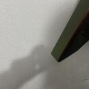 Detailní záběr na hranu tmavě zeleného nástroje s kovovým prvkem v horní části. Povrch je matný a bez viditelných značek či nápisů.
