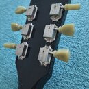 Zadní strana černé hlavy kytary s šesti ladicími mechanismy. Na kovových částech ladíček je vyryto slovo GIBSON a DELUXE. Ladicí kolíky jsou vyrobeny…