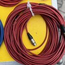 Červený kabel sletovaný do kruhu a stahovadlem z bílého plastu. Na koncích jsou vidět kovové konektory typu XLR. Kabel leží na žlutém povrchu vedle m…
