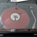 Černý gramofon s průhledným plastovým krytem, na kterém je položena červená vinylová deska. Na spodní hraně přístroje je bílý nápis Pioneer DJ DIRECT…