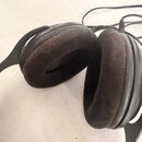 Černé uzavřené sluchátka s hnědými látkovými náušníky. Na vnější straně pravého náušníku je viditelný nápis "SONY". Sluchátka jsou připojena k černém…