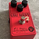 Červený kytarový efekt s nápisem BIG MUFF Pi 2 a DUAL OP-AMP. Na spodní části je logo electro-harmonix, podpis R.E. Myer a nápis NEW YORK CITY, USA s…