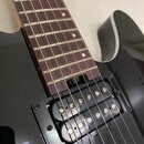 Detail elektrické kytary s černým bodies a hnědým hmatníkem z tmavého dřeva. Na těle je instalován černý humbucker snímač s viditelnými polkovými mag…