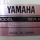 Kovový štítek s nápisem YAMAHA v horní části. Uprostřed je černý pruh s bílými nápisy MODEL a SER. NO., pod kterým je vyražen text RECORDING. Ve spod…