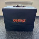 Černý textilní kryt na hudební zesilovač nebo kombo s rukojetí na horní straně. Uprostřed je oranžový nápis ORANGE. Povrch látky vykazuje mírné pomač…