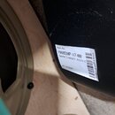 Detail černé povrchové vrstvy skříně reproduktoru s bílou nálepkou. Na nálepce je uveden text: Item No 1960EMP-17-00, 1960BX CABINET ASSY-E a WO 2578…