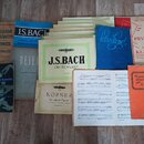 Sestup rozložených notových sešitů a knih na dřevěné podlaze. Jsou zde tituly jako „Základové hry klavírní“ (Prof. H. TRNECEK, Prof. K. HOFFMEISTE),…