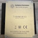 Zadní strana kovového zařízení stříbrné barvy. V horní části je logo a nápis Darkglass Electronics Your vision, our gear. Uprostřed je uveden SERIAL…