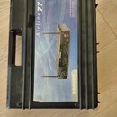 Černý plastový přepravní kufr s rukojetí. Na víku je nalepený papírový štítek s nápisy „Airline 77“, „UHF TRUE DIVERSITY WIRELESS SYSTEM“ a logem „SA…