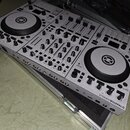 Stříbrný DJ kontrolér umístěný v transportním kufru. Na spodní hraně je nápis TRAKTOR KONTROL S4. Zařízení má dvě velké ovládací jog-kola s logem v c…