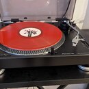Černý turntable Pioneer DJ s nápisem DIRECT DRIVE TURNTABLE PLX-500. Na talíři je umístěna červená vinylová deska s bílým štítkem. Přístroj je vybave…