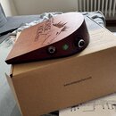Hnědý dřevěný perkusní nástroj s vyrytým profilem koně a nápisy ORTEGA, HORSE KICK PRO. Na boku jsou umístěny dva konektory a zelená kulatá nálepka s…