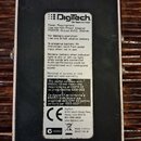 Zadní strana efektového pedálu s černým povrchem a kovovým rámem. Uprostřed je bílá nálepka s nápisem Digitech The Power to Create a technickými spec…