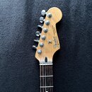 Hlava a hриф elektrické kytary s tmavým hmatníkem. Na hlavě je viditelné logo Fender, nápis STRATOCASTER a text MADE IN MEXICO. Pod nimi je uveden kó…