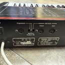 Zadní strana černé klaviatury s několika konektory. Jsou zde nápisy POWER, Programmer, MIDI BUS Output a Input, a Memory Protect On. Na stříbrném ští…