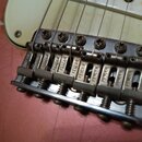Detailní záběr na kovový kobylkový systém elektrické kytary s bílým pickguardem. Na šesti sedly je vyryt nápis FENDER. Kovové části vykazují známky o…