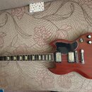 Elektrická kytara s červeným dřevěným povrchem a černým plechtrátem. Na hlavě je viditelné logo Epiphone a nápis 80. Kytara má dva humbuckery, čtyři…