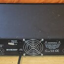 Černý rackový zesilovač s nápisy CHANNEL 1 a CHANNEL 2. Na zadním panelu je logo BVaudio, nápis XLR INPUT a varovný text WARNING DANGEROUS VOLTAGE IN…