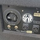 Záběr na zadní ovládací panel černého reproduktoru. Panel obsahuje regulační knoflík s nápisem LEVEL CONTROL a HIGH, dva konektory INPUT a OUTPUT ora…
