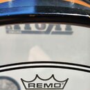 Detail bubnové membrány s nápisem REMO, POWERSTROKE P3 CLEAR a MADE IN U. S. A. Membrána je průhledná s černými vnějšími kruhy. V horní části je vidě…