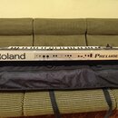 Digitální klavír v stříbrném provedení s černými detaily, položený na černé přepravní tašce. Na levé straně je vidět nápis Roland a na pravé straně n…
