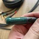 Detailní záběr na konektor kabelu v zelené barvě. Na povrchu je vyražen nápis NEUTRIK. Konektor je zakončen černým plastovým krytem a je připojen k č…