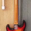 Zadní strana elektrické kytary s trupem v červeno-žlutém přechodovém lakování (sunburst). Na kovové spojovací desce u krku je nápis "STRATOCASTER" a…
