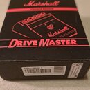 Černá krabice s červenými nápisy a lineárními prvky. Na horní straně je logo Marshall, text VINTAGE REISSUE a název DRIVE MASTER spolu s červenou čar…