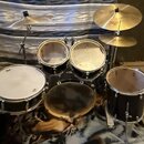 Sada bubnů v černé barvě s kovovými obručemi a dvěma cymbály. Na horním cymbálu je viditelné logo Pearl. Povrchy blan bubnů vykazují známky opotřeben…