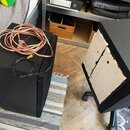 Na fotografii jsou dva černé reproduktory v interiéru. Na horní části jednoho z nich leží srolovaný růžový kabel a černý kabel. Druhý reproduktor je…