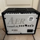 Zadní strana akustického komba v černém krytu. Na bílém panelu je velký šedý nápis AER a pod ním černý text Compact 602 twin channel acoustic amplifi…