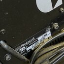 Detailní záběr na zadní stranu černého hudebního zařízení s viditelným typovým štítkem. Na štítku je logo a nápis Roland, specifikace AC 230 V~ 50/60…
