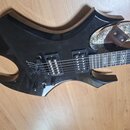 Černá elektrická kytara s výrazně hranatým, atypickým tvarem těla. Nástroj má dva humbuckery a fixační kobylku sáhlající přes tělo. Na hředníku jsou…
