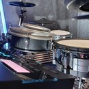 Elektronická bicí souprava s několika padovými bubny v černé barvě a kovovými obručmi. Na jednom z padů je vidět logo Roland, nápis V-Drums a označen…